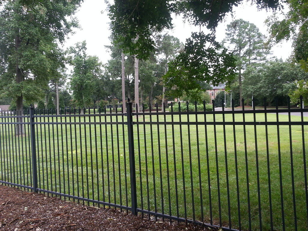 Black ornamental metal picket fence with spear-top finials along a lawn, shown as a style example of the ornamental aluminum fencing look